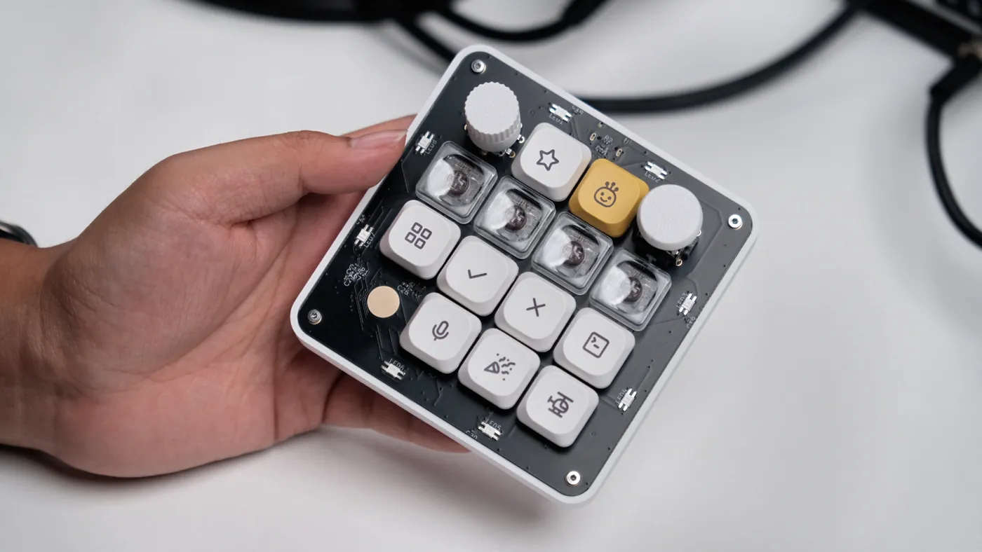 The finished OpenMicroKbd held in one hand: black PCB in a white printed case, icon keycaps, a knob, a joystick and a yellow accent key